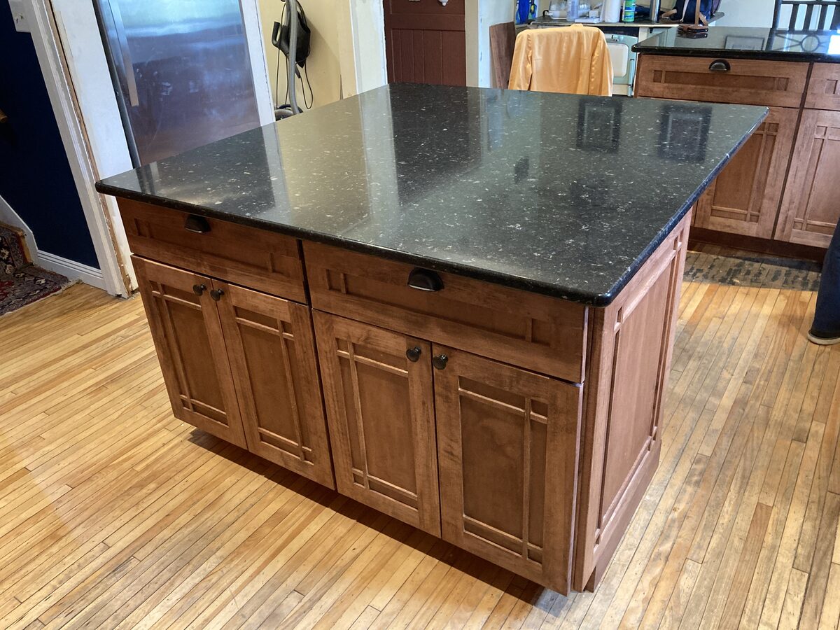 Custom craftsman-style kitchen island with dark countertop and panel door details