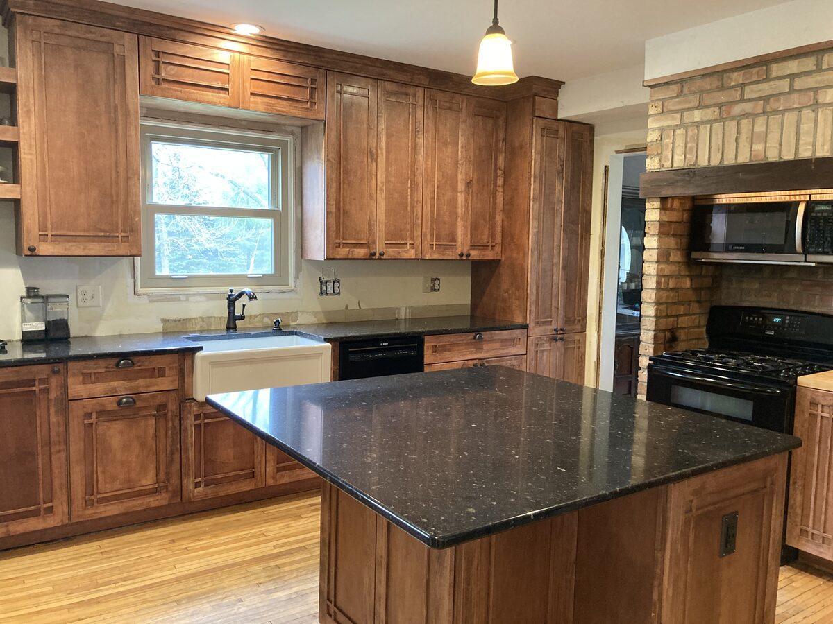 Full kitchen remodel with custom craftsman-style brown cabinets, black granite countertops, and farmhouse sink
