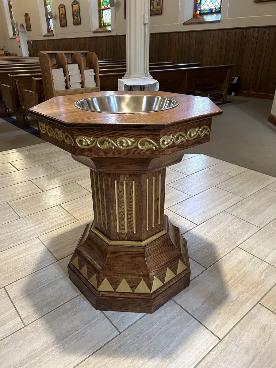 Baptismal font with gold scroll detailing installed in church with stained glass windows and pews
