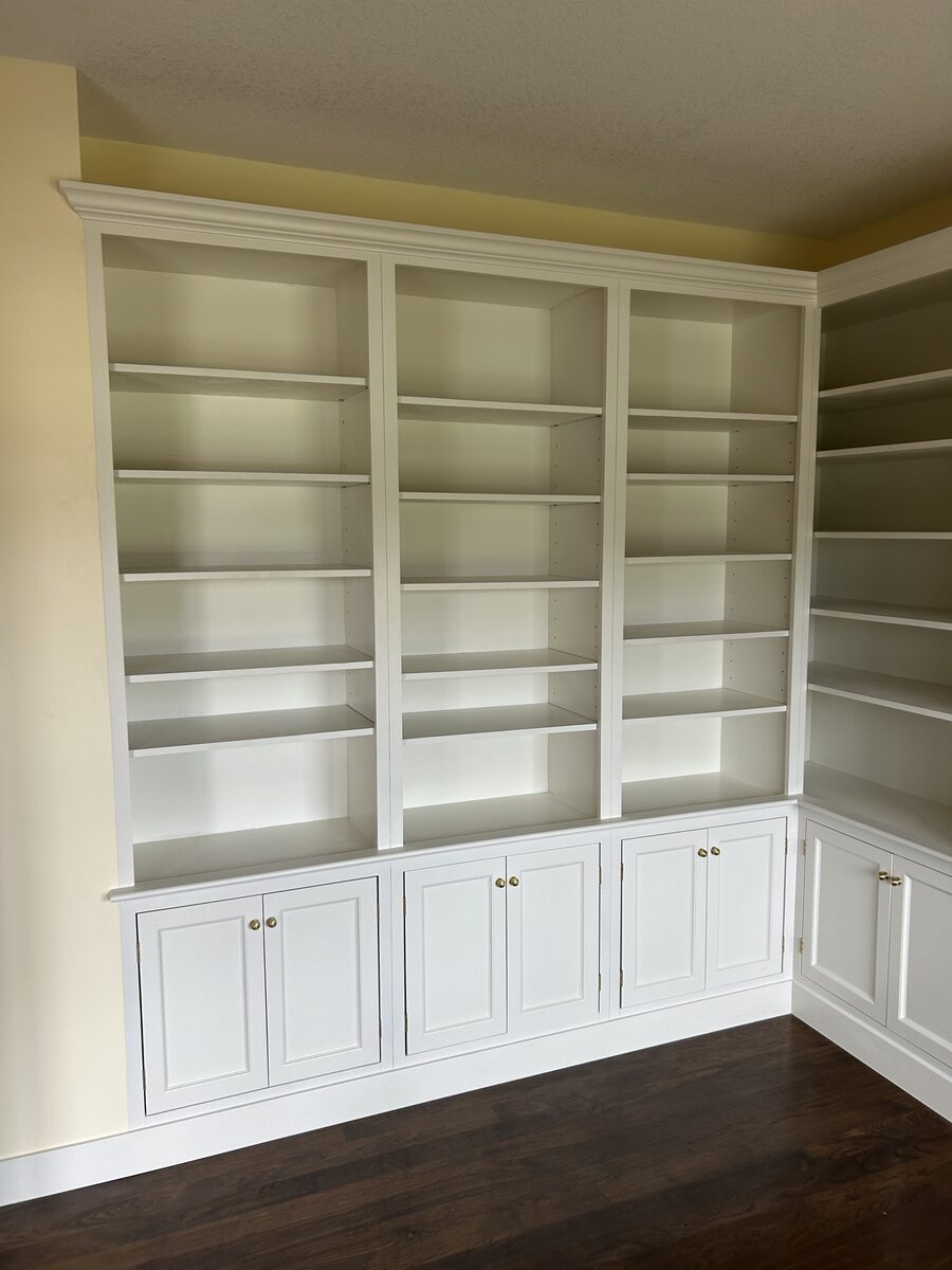 Floor-to-ceiling white built-in bookshelves with lower cabinets and crown molding