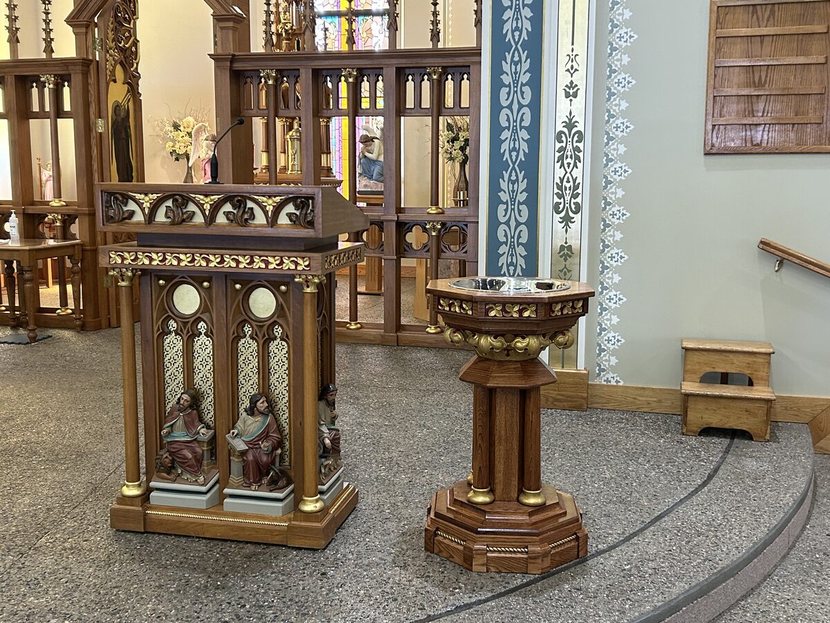Gothic-style ambo with carved evangelist figures and baptismal font with gold leaf installed in a church sanctuary