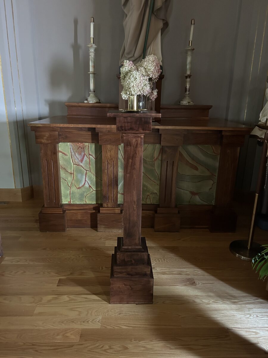 Custom walnut ambo installed in a chapel with backlit altar panels and candles