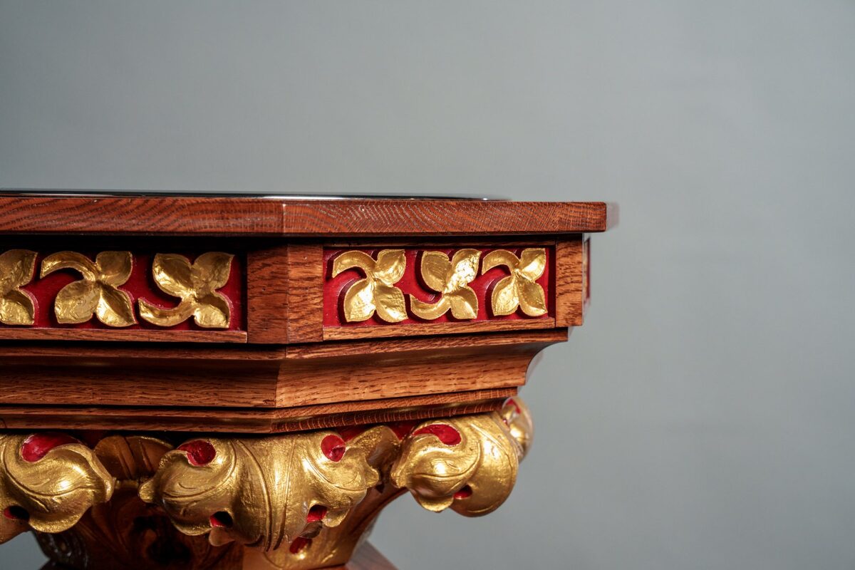 Baptismal font close-up showing hand-carved gold leaf trefoil panels with red backing